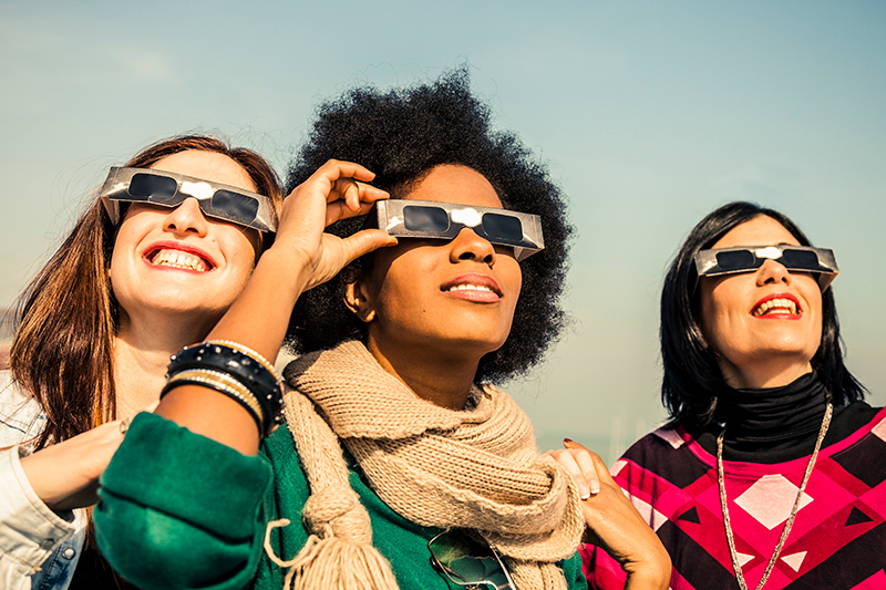 three woman watching the eclipse wearing eclipse glasses
